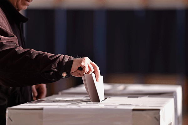 person inserting ballot in voting box 600x400